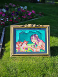 Framed artwork of a woman and cat on grass with flowers in the background.