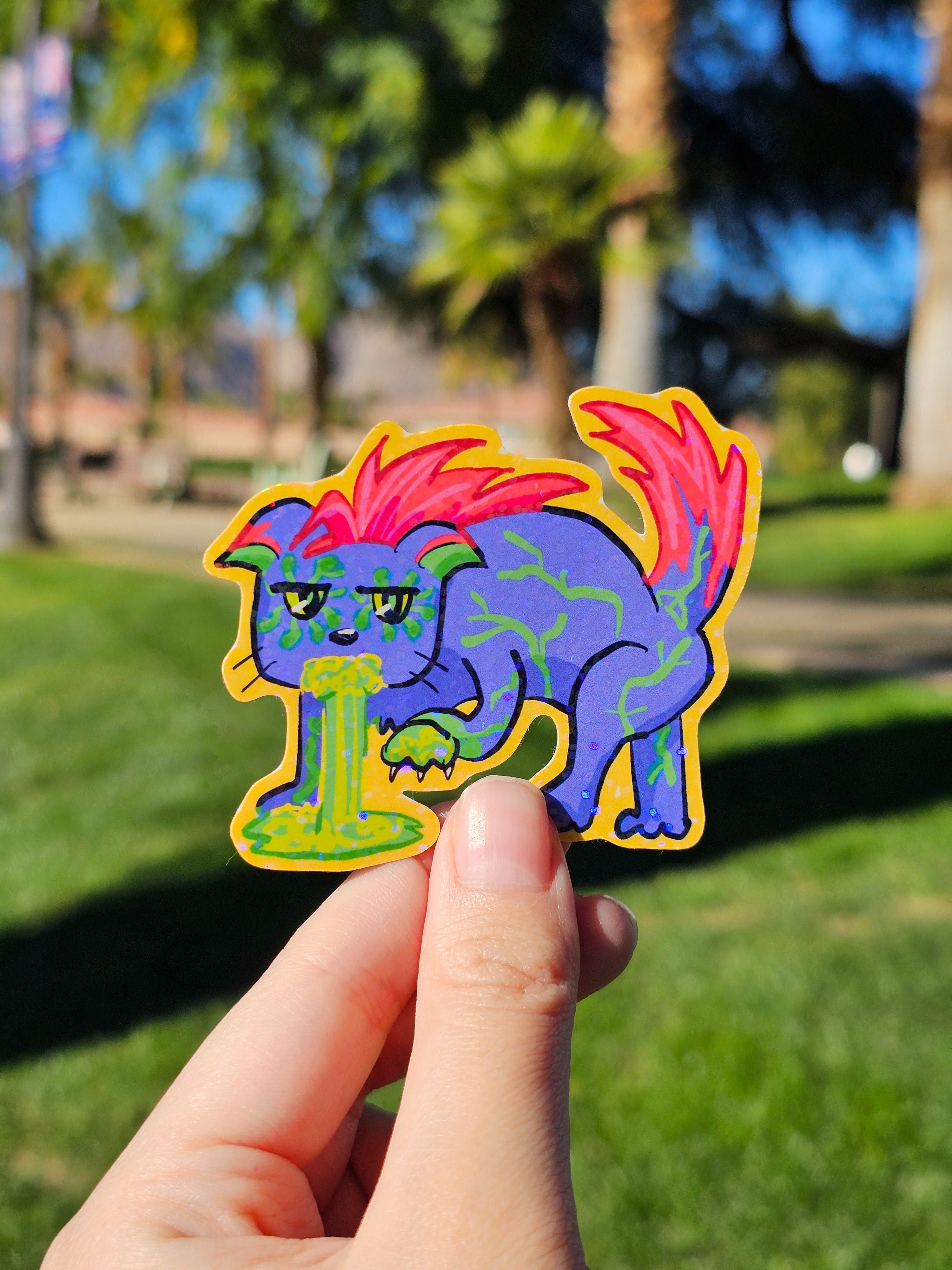 Colorful cartoon-style sticker of a cat vomiting toxic waste held in front of a park background
